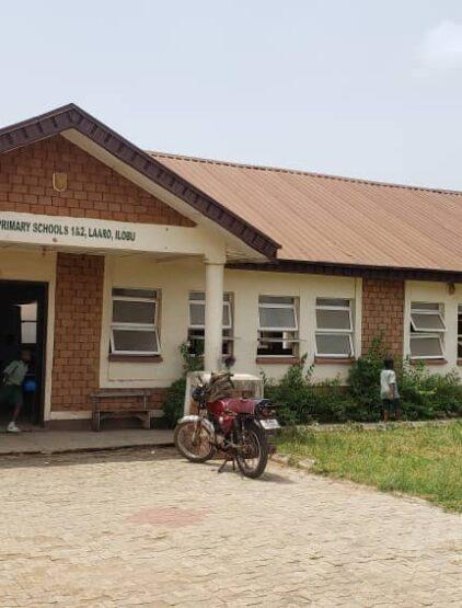 Primary Schools 1 and 2 at Laaro, a pupil in the doorway and a motorcycle parked under the eaves.